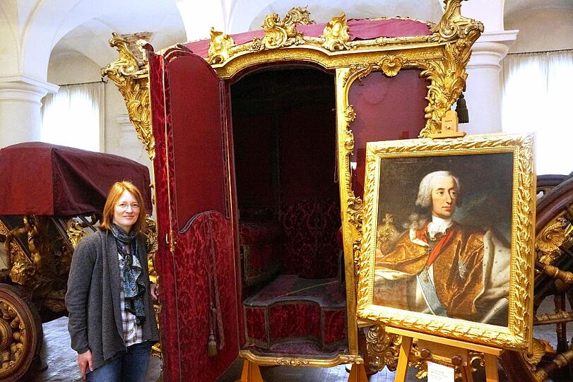 Bitte einsteigen: Kuratorin Friederike Ulrichs öffnet die Tür zum Krönungswagen, daneben ein Bildnis von Kaiser Karl VII.