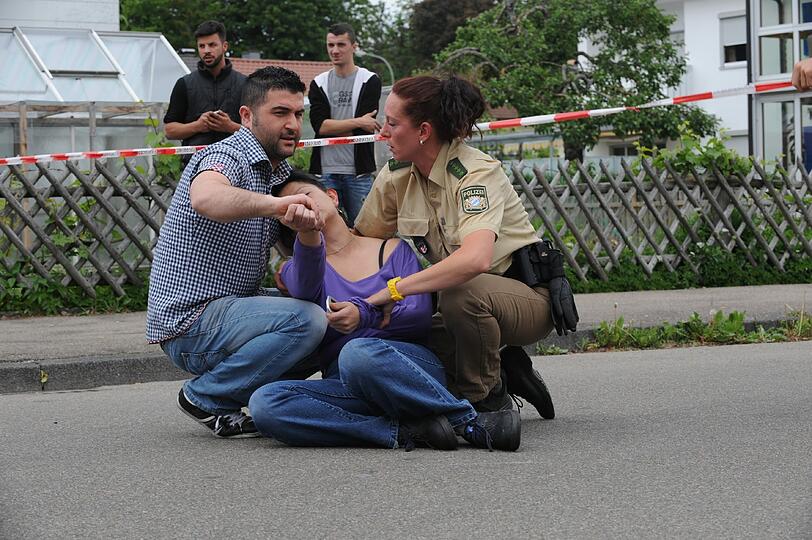 Polizisten helfen vor einer Mittelschule in Memmingen der ohnmächtigen Mutter einer Schülerin, nachdem in der Schule um die Mittagszeit ein Schuss gefallen ist (Foto vom 22.05.12).