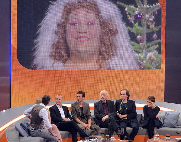 Moderator Markus Lanz (v.l.) sitzt am neben seinen Gästen Helene Fischer, Heino Ferch, Florian David Fitz, Karl Dall, Olaf Schubert und Nena (Gabriele Susanne Kerner) vor einem Bild von Assistentin Cindy aus Marzahn (Ilka Bessin)
