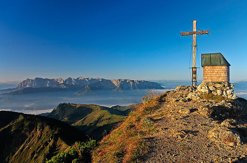 Der Gipfel des Geigelsteins in den Chiemgauer Alpen. Im Hintergrund spitzt das Kaisergebirge durch die Nebelschwaden.
