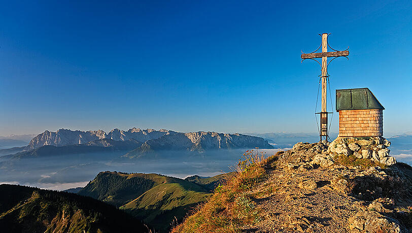 Der Gipfel des Geigelsteins in den Chiemgauer Alpen. Im Hintergrund spitzt das Kaisergebirge durch die Nebelschwaden. Der Gipfel des Geigelsteins in den Chiemgauer Alpen. Im Hintergrund spitzt das Kaisergebirge durch die Nebelschwaden.