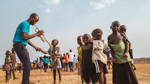 Musiklehrer Ssali Deogratious mit seiner neuen Callet-Trompete beim "Community Music"-Marsch in der Flüchtlingssiedlung Bidi Bidi in Uganda bei der Arbeit: Der helle, strahlende, luzide Klang des Instruments aus München fasziniert Kinder.