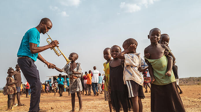 Musiklehrer Ssali Deogratious mit seiner neuen Callet-Trompete beim "Community Music"-Marsch in der Flüchtlingssiedlung Bidi Bidi in Uganda bei der Arbeit: Der helle, strahlende, luzide Klang des Instruments aus München fasziniert Kinder.