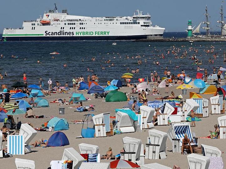 Urlauber suchen an der Ostsee in Warnemünde nach Abkühlung, während die Scandlines-Fähre "Berlin" einläuft.