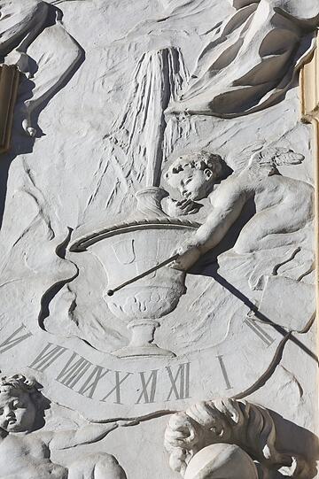 Am Asamhaus hat dieser kleine Engel einen Stab in der Hand und zeigt so die Uhrzeit auf einer Sonnenuhr.