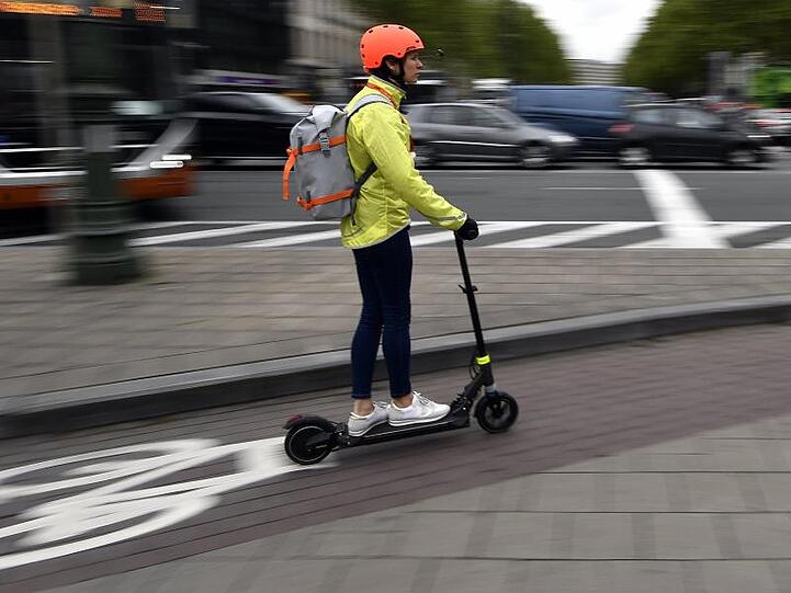 Ein Frau fährt auf einem E-Tretroller auf einem Fahrradweg.