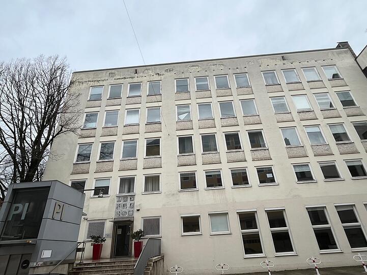 Das Pädagogische Institut von der Rückseite an der Marienstraße aus gesehen. Die Reliefs über dem Eingang zeigen Buchstaben, die Fenster sind mit hellen Steinen unterfangen.