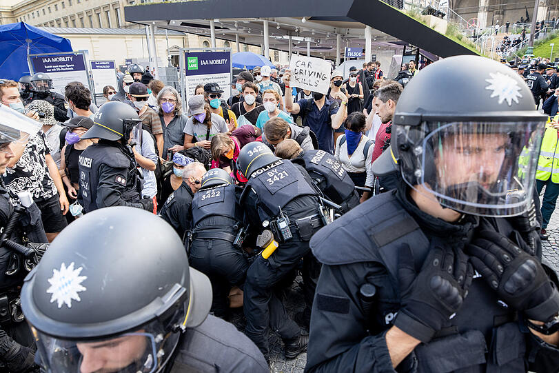 Polizisten nehmen am Odeonsplatz eine Person fest, während Aktivisten den Stand von Mercedes blockieren.