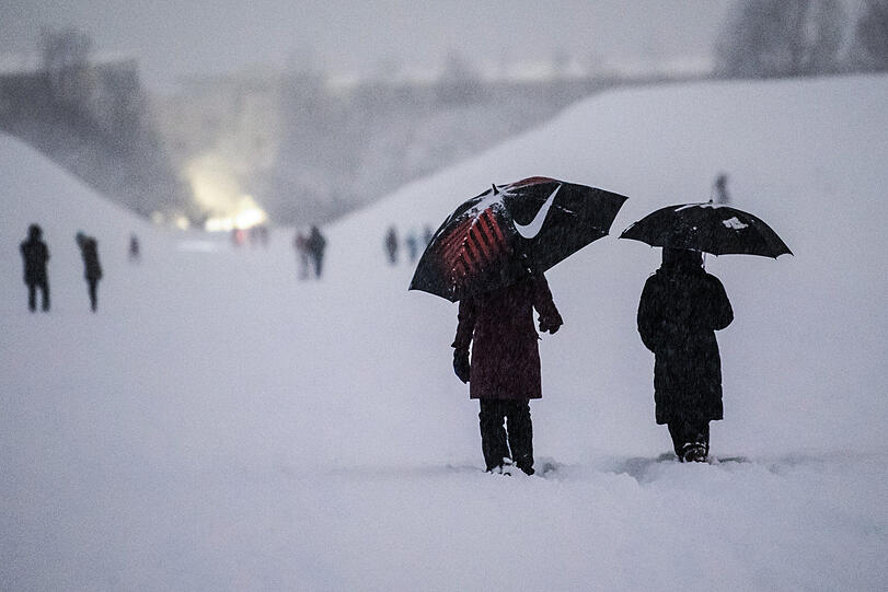 Spaziergänger gehen mit Regenschirmen durch den stark verschneiten Landschaftspark Hachinger Tal.