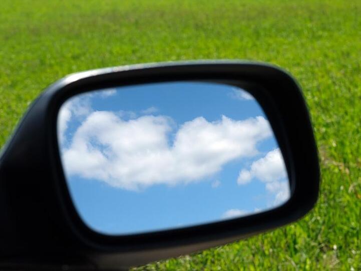 Blauer Himmel und Wolken im Außenspiegel eines Autos.
