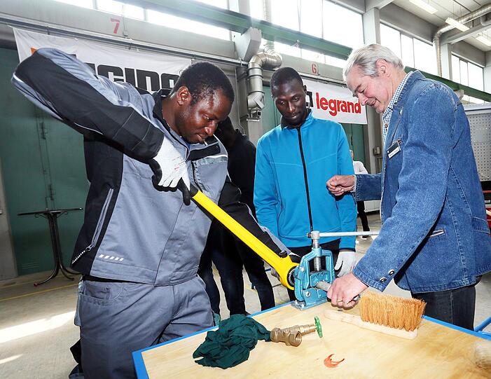 Hochkonzentriert: Meister Wilhelm Thalmayer (66,r.) zeigt Basasay Dibasey (29, M.) aus Sierra Leone und Gawiara Barama (30) aus dem Senegal, wie man ein Gewinde in ein Rohr schneidet.