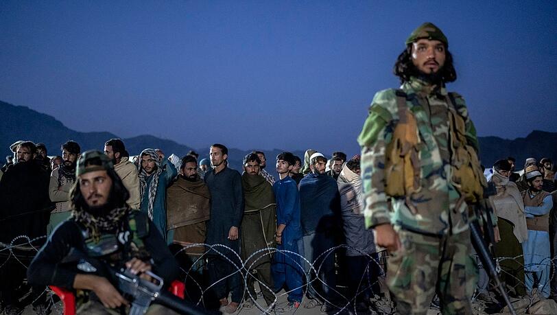 Taliban-Kämpfer stehen Wache, während afghanische Flüchtlinge in einem Lager nahe der pakistanisch-afghanischen Grenze anstehen, um sich registrieren zu lassen.