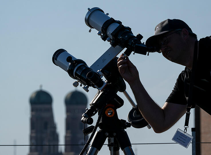 Ein Hobby-Astronom richtet sein Teleskop auf der Dachterrasse des Kulturzentrums Gasteig ein, um am Abend die partielle Sonnenfinsternis zu beobachten. Im Hintergrund sind die beiden T&uuml;rme der Frauenkirche zu sehen.