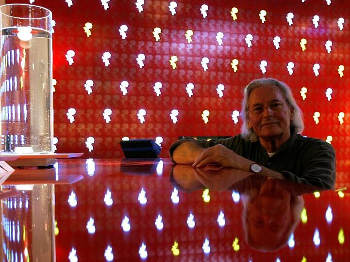 Der Münchner Designer Ingo Maurer steht neben der Designlampe "Delirium Yum" (links) und vor einer LED-Wand mit Rosenmotiven. Foto: Arne Dedert/dpa/Archivbild