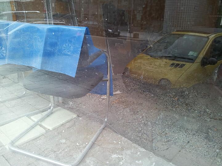 Im Schaufenster stehen zwei Stühle. Im Fenster spiegelt sich der Schörghuber-Komplex gegenüber. Dort floriert das Geschäft: Saturn, XXXLutz und Toys'R'Us betreiben Filialen.
