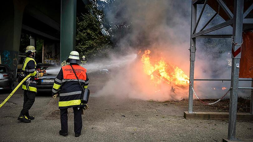 Feuerwehrkräfte mit schwerem Atemschutz löschen den Wohnwagen unter der Eisenbahnbrücke in Untergiesing.
