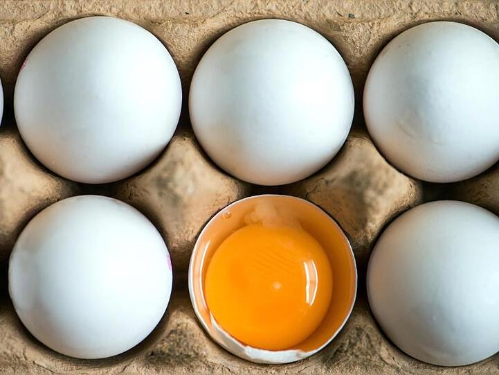 Ein aufgeschlagenes Ei liegt zwischen anderen weißen Eiern in einem Karton. Foto: Armin Weigel/dpa/Symbolbild