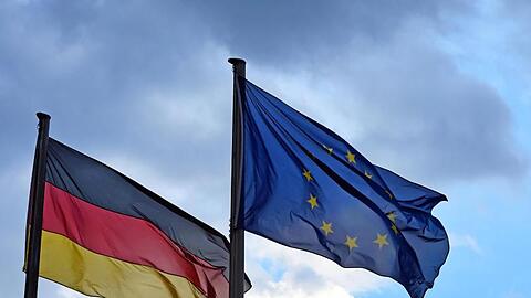 Eine Deutschland- und eine EU-Fahne vor wolkigem Himmel. Nach Ansicht von Günther Oettinger sollten Bundesminister künftig hauptsächlich in Brüssel oder Luxemburg arbeiten.