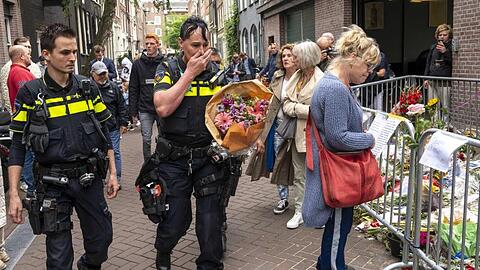 Polizisten bringen einen Blumenstrauß zu dem Blumenmeer für den Reporter Peter R. de Vries in der Leidswarsstraat.