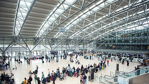 Reisende stehen im Terminal des Flughafens Hamburg in einer Warteschlange an einem Check-in-Schalter.