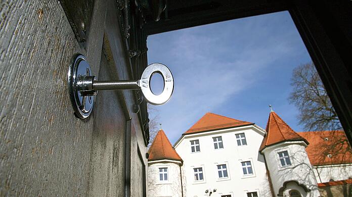 Im Schloss der geöffneten Türe des Eingangsbereiches der Justizvollzugsanstalt in Aichach steckt ein Schlüssel. Ein Beamter des Gefängnisses wurde nun zu einer Geldstrafe verurteilt, weil er einen Insassen geschlagen hatte. (Archivbild-Illustration)