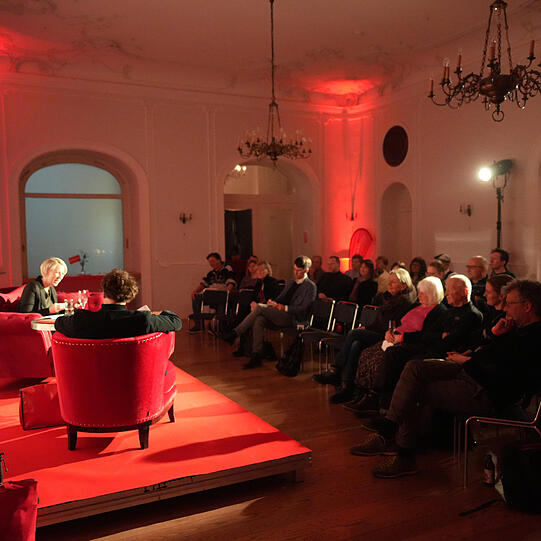 Adrian Prechtel im Gespräch mit Bürgermeisterin Katrin Habenschaden auf dem roten Sofa (von Möbel Höffner) in München.