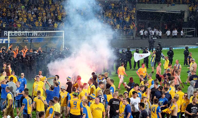 Braunschweiger Fans stehen Polizisten und Ordnern nach dem Abpfiff auf dem Platz gegenüber.