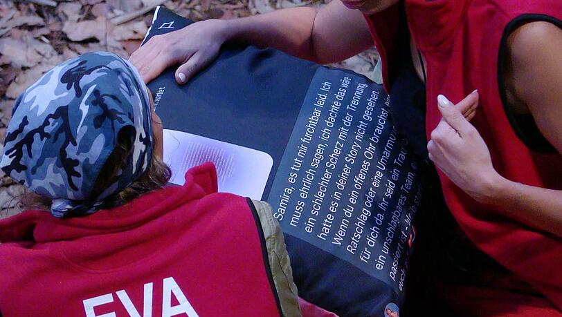 Die Kissenbombe platzt: Eva bekommt von Samira den Text auf ihrem bedruckten Kissen vorgelesen.