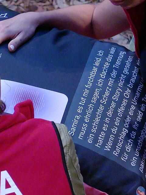 Die Kissenbombe platzt: Eva bekommt von Samira den Text auf ihrem bedruckten Kissen vorgelesen.