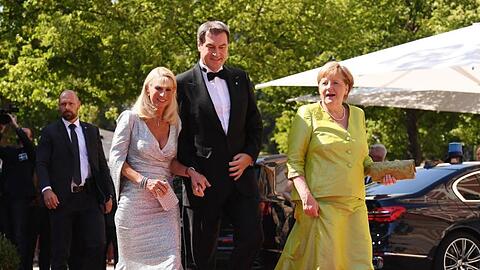 Bundeskanzlerin Angela Merkel schreitet mit dem Bayerischen Ministerpräsidenten Markus Söder und dessen Frau, Karin Baumüller-Söder, über den roten Teppich.