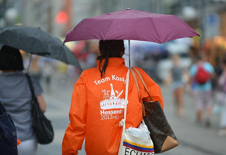 Hessentagsbesucher mühen sich am 20.06.2013 in Kassel (Hessen) im Gewitterregen ab, einen Plastik-Regenschutz anzulegen. Ein Gewitter zog am Nachmittag über die Stadt und vertrieb die größte Hitze.