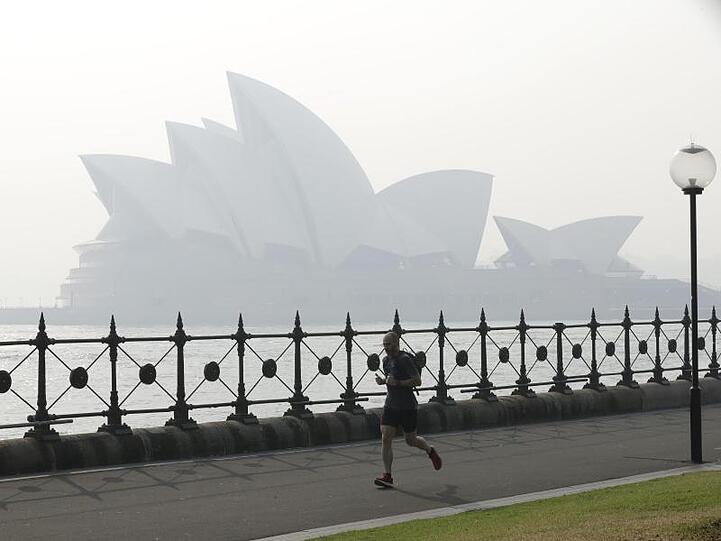 Ein Jogger läuft am Morgen, während Rauchschleier über der Sydney Opera House hängt.