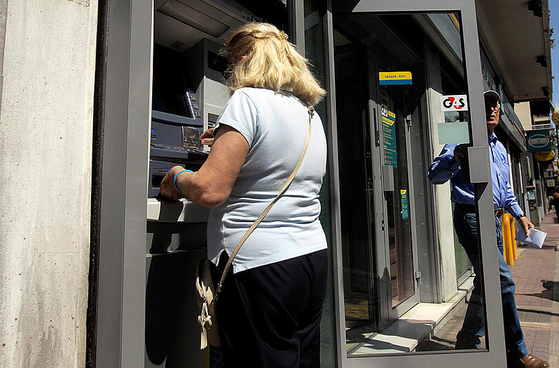 Eine Frau in Athen hebt Geld an einem Automaten ab. Immer mehr griechische Verbraucher ziehen Bank-Einlagen in großer Höhe ab.