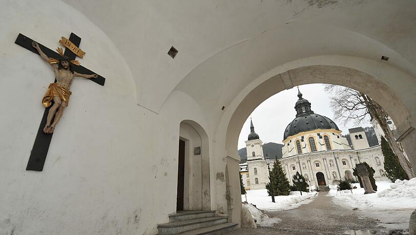 Durch den Eingang zum Kloster Ettal im Landkreis Garmisch-Partenkirchen ist die Kloster- und Pfarrkirche zu sehen. Durch den Eingang zum Kloster Ettal im Landkreis Garmisch-Partenkirchen ist die Kloster- und Pfarrkirche zu sehen.