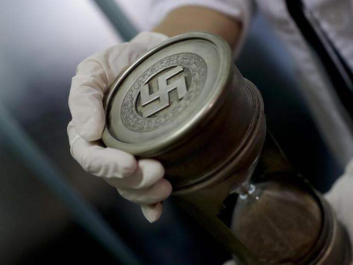 Ein Mitglied der Bundespolizei hält am 16.06.2017 im Interpol-Hauptquartier in Buenos Aires (Argentinien) eine Sanduhr mit Hakenkreuz. Das Auktionshaus Hermann Historica versteigert ähnliche Nazi-Devotionalien.