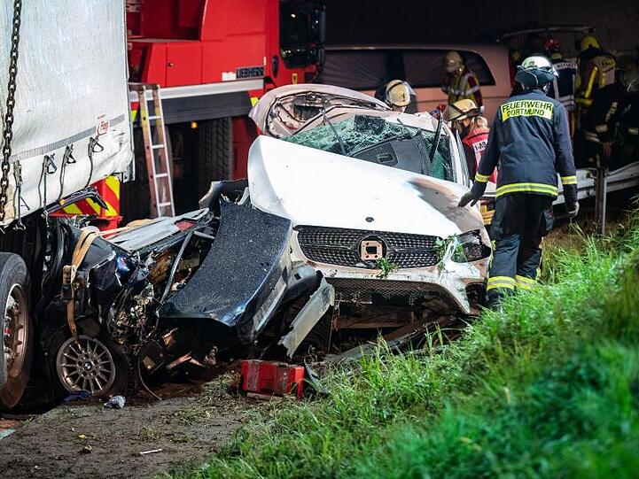 Einsatzkräfte der Feuerwehr stehen auf der A2 neben völlig zerstörten Fahrzeugen.