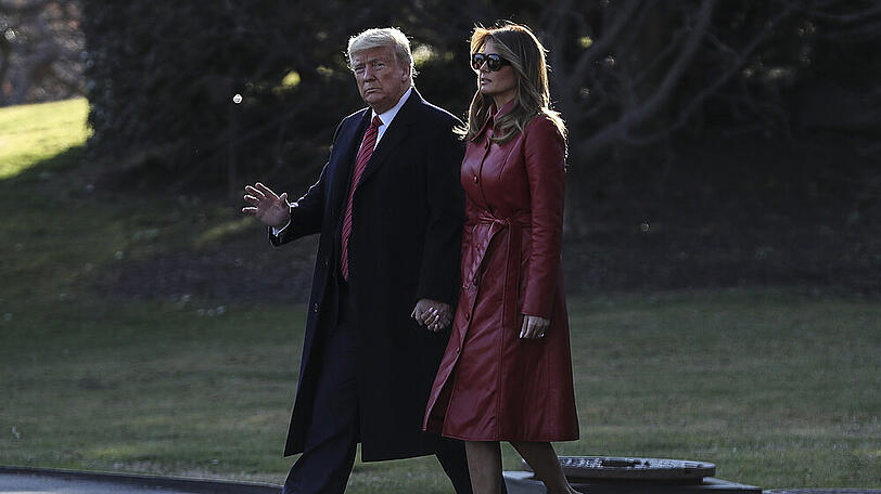Melania Trump im roten Kunstleder-Trenchcoat an der Seite von Donald Trump.