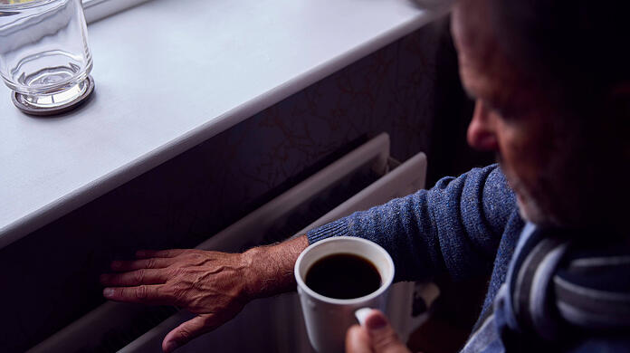 Ein Mann fühlt an den Heizkörper, um zu testen, wie warm er ist. Wer Kosten sparen will, neigt dazu, weniger zu heizen.