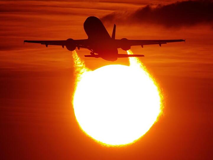 Ein Flugzeug startet am Flughafen in Düsseldorf vor der untergehenden Sonne.