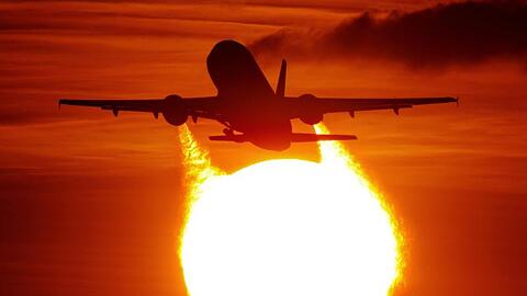 Ein Flugzeug startet am Flughafen in Düsseldorf vor der untergehenden Sonne.