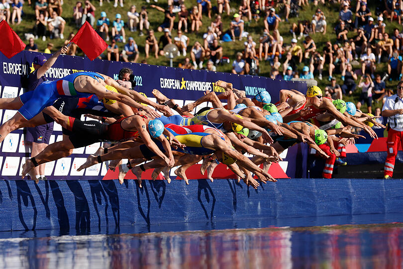 Triathlon-Start im Olympiapark. Im Hintergrund schauen die Besucher auf dem Olympiaberg zu.