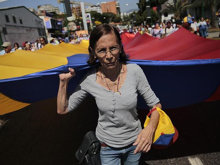 Eine Frau trägt bei der Protestkundgebung der Opposition gemeinsam mit anderen Demonstranten eine große venezolanische Flagge.