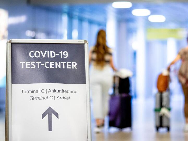 Ein Schild weist Reisende in einem Flughafen auf das Corona-Testzentrum hin.