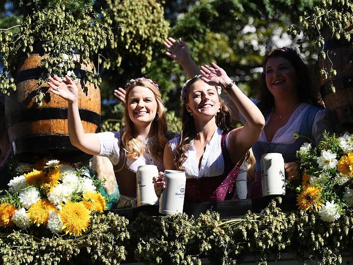 Bedienungen und Gäste feiern beim Einzug der Wiesenwirte zum Oktoberfest auf einer geschmückten Kutsche.