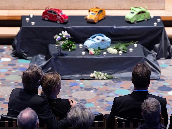 Trauernde sitzen bei der Gedenkfeier für Heidi Hetzer in der Kaiser-Wilhelm-Gedächtnis-Kirche. Auf einem niedrigen Podest sind die Handtaschen der Verstorbenen im Auto-Design neben Kerzen aufgestellt.