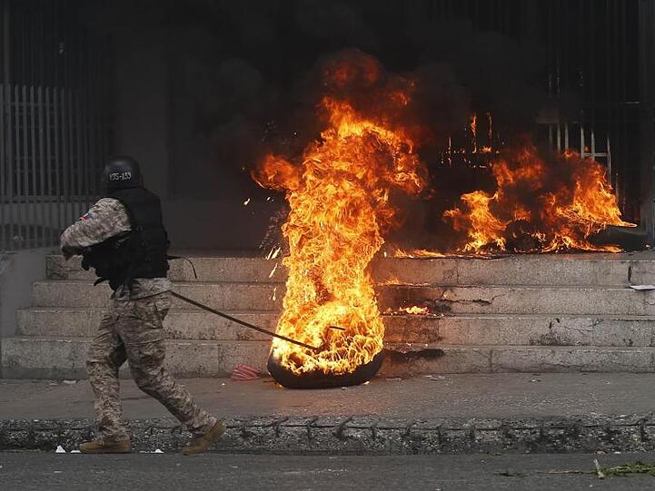 Ein Polizist entfernt einen brennenden Reifen vor einem Regierungsgebäude. Bei den Protesten gegen Haitis Regierung ist es in der Hauptstadt Port-au-Prince zu schweren Krawallen gekommen.
