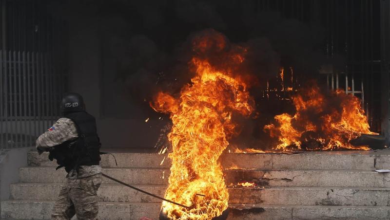 Ein Polizist entfernt einen brennenden Reifen vor einem Regierungsgebäude. Bei den Protesten gegen Haitis Regierung ist es in der Hauptstadt Port-au-Prince zu schweren Krawallen gekommen. Ein Polizist entfernt einen brennenden Reifen vor einem Regierungsgebäude. Bei den Protesten gegen Haitis Regierung ist es in der Hauptstadt Port-au-Prince zu schweren Krawallen gekommen.