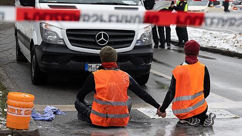 Zwei Klimaaktivisten der "Letzten Generation" versuchen, sich auf einer Straße in München trotz Nieselregen und Minusgraden festzukleben.