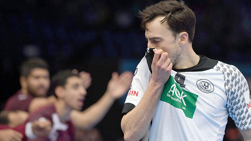 Deutschlands Patrick Groetzki wischt sich sein Gesicht am Trikot ab, während Spieler aus Katar im Hintergrund jubeln.