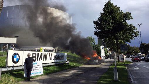 Protest bei BMW: Mit Plakat und brennendem Auto will Pourmohseni sich Gehör verschaffen. Foto: Regine Kruzinna Protest bei BMW: Mit Plakat und brennendem Auto will Pourmohseni sich Gehör verschaffen. Foto: Regine Kruzinna